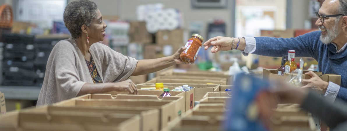 Small group of people donating their time by working in a warehouse to organize and distribute non-perishable goods to families and people in need.